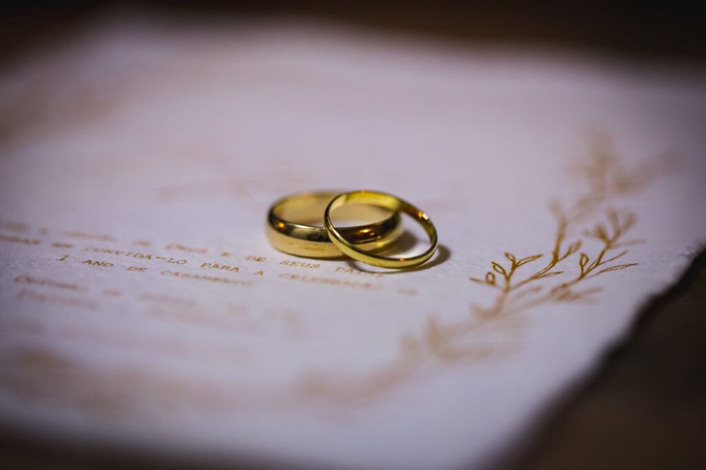 Two gold wedding rings resting on an elegant wedding invitation.